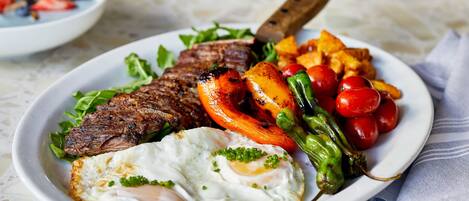 Une assiette de nourriture comprenant un steak, des œufs et des légumes.