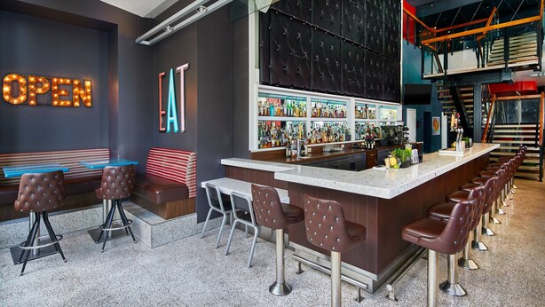 A bar area with a long counter, multiple stools, and a seating area with a bench. - Courtyard by Marriott Portland City Center (Portland)