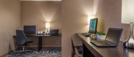 A hotel room with a desk, two chairs, a laptop, a desktop computer, a printer, and a lamp.
