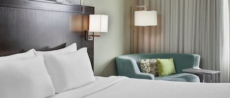 A hotel room with a large bed, a green armchair, a small table, and a wall-mounted lamp.