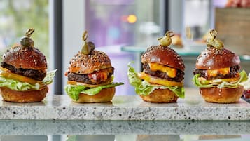 Quatro hambúrgueres gourmet com sementes de gergelim e detalhes decorativos sobre uma bancada de mármore.