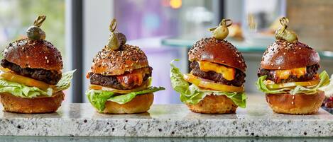 Cuatro hamburguesas gourmet con semillas de sésamo y detalles decorativos sobre una encimera de mármol.