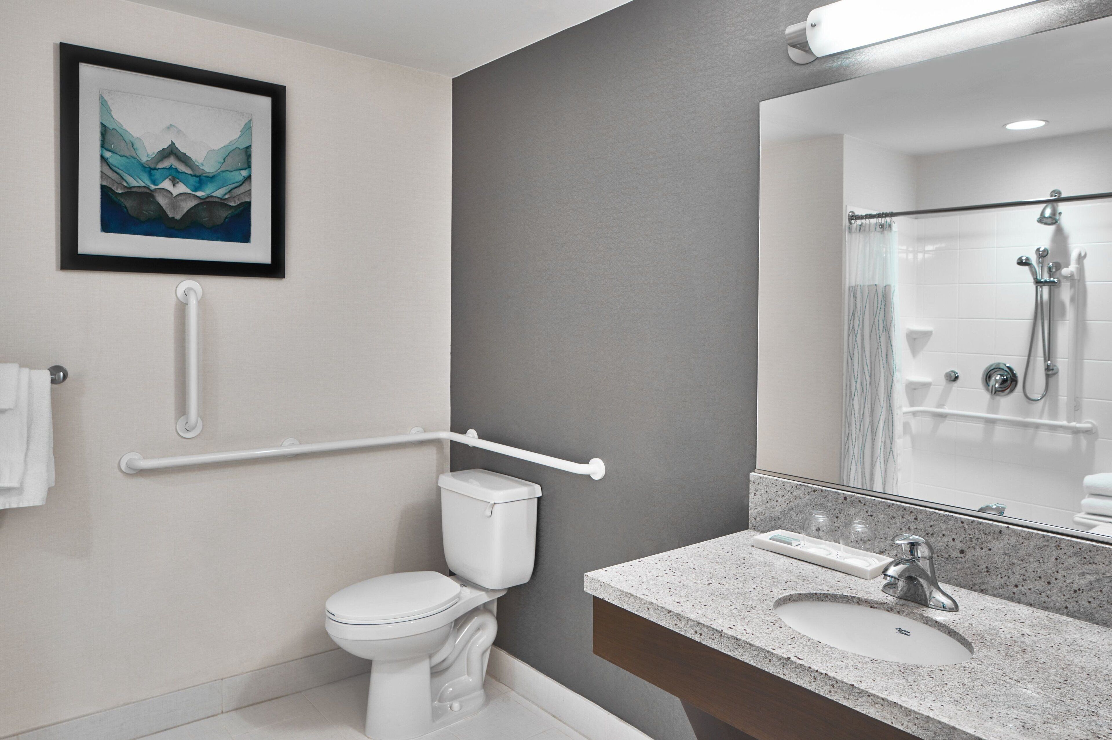 Un baño moderno con inodoro blanco, lavamanos con espejo y zona de ducha.