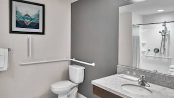 Un baño moderno con inodoro blanco, lavamanos con espejo y zona de ducha.