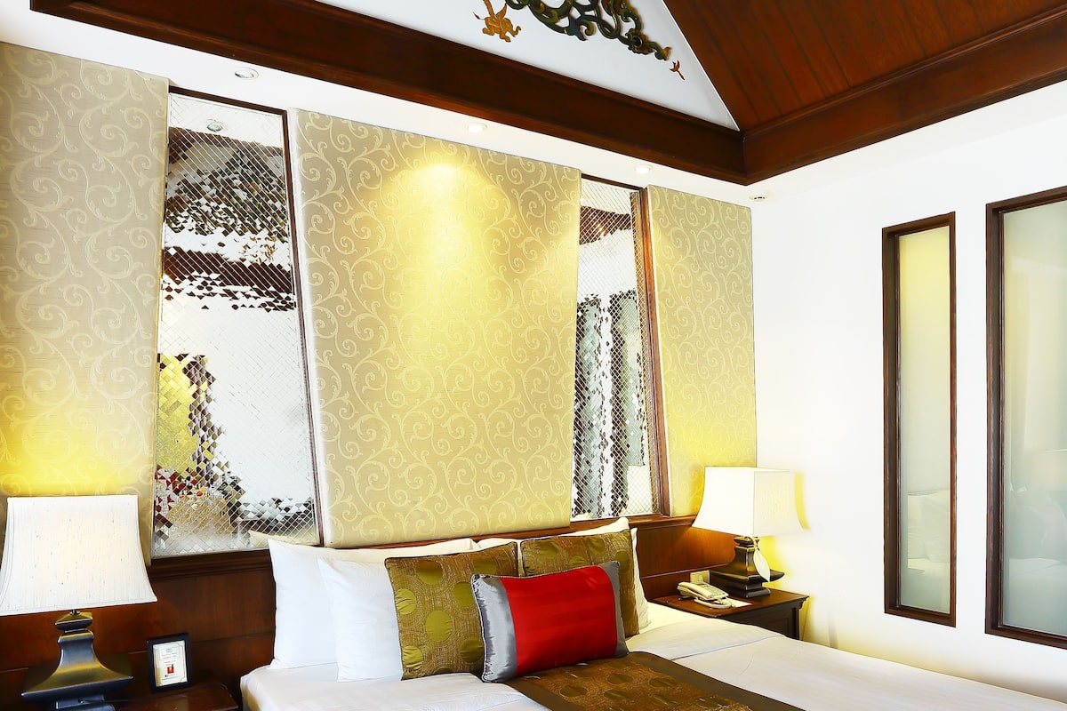 A hotel room with a large bed, wooden headboard, two bedside tables with lamps, and a decorative ceiling piece.