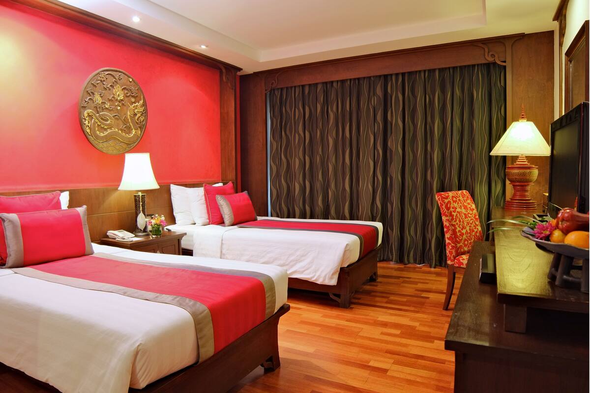 A hotel room with two beds, a desk, a chair, a lamp, and a curtain.