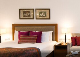Habitación de hotel con una cama, dos mesitas de noche, una silla y dos cuadros enmarcados.