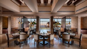 A spacious restaurant with multiple dining areas, large windows, and a modern interior design. - Jaypee Residency Manor (Dehradun)