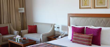A hotel room with a large bed, two armchairs, a small table, and a nightstand. There are two framed pictures on the wall above the bed.