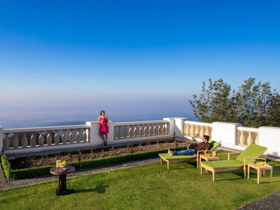 A rooftop terrace with a clear view of the horizon, a white balustrade, and a small table with flowers.