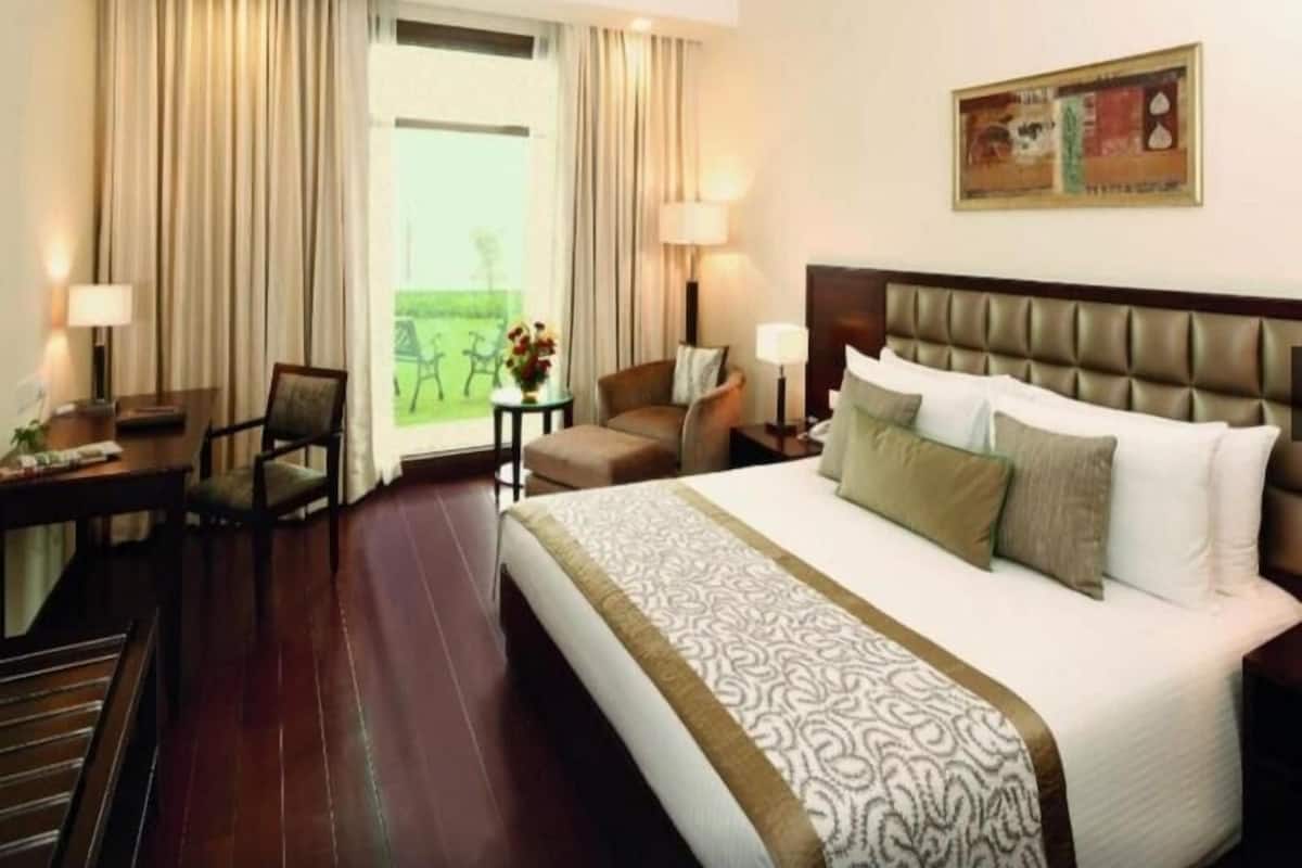 A hotel room with a large bed, a desk, a chair, and a view of the outdoors.