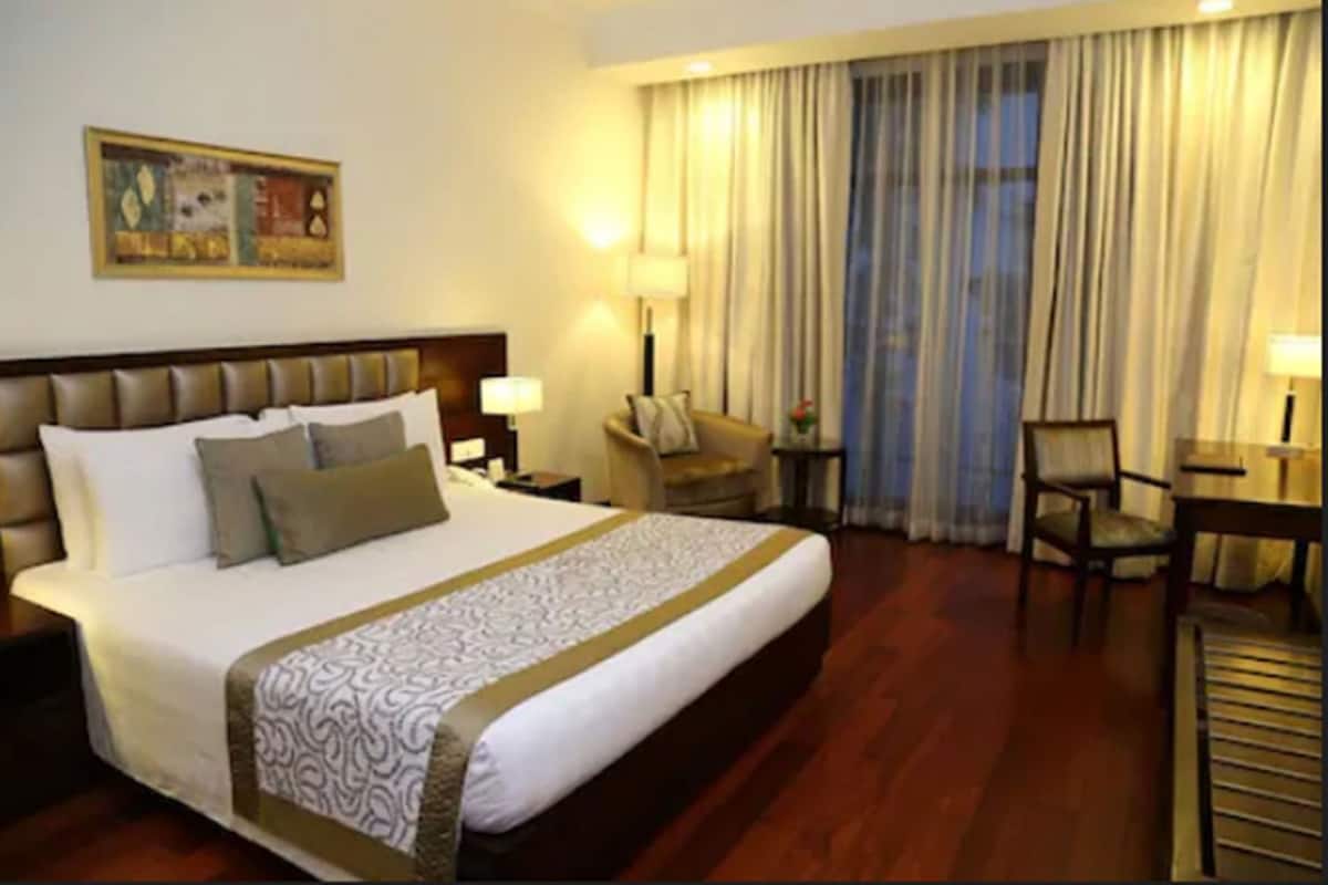A hotel room with a large bed, a desk, a chair, a nightstand, and a painting on the wall.