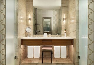A modern bathroom with a large mirror, two sinks, and a bench.