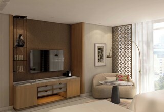 A modern hotel room with a large flat-screen TV, a sofa, a round coffee table, and a decorative wall panel.