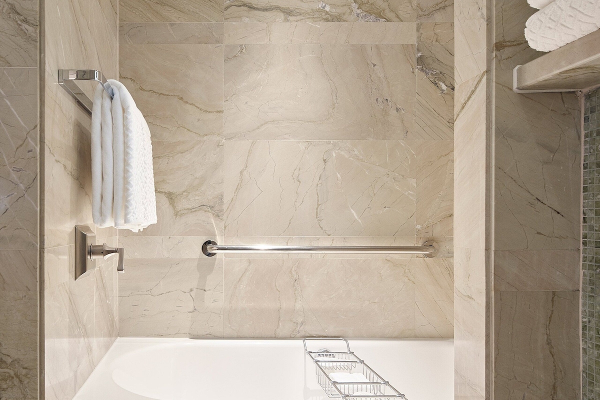 A modern bathroom with a marble wall, a bathtub, and a glass shower enclosure.