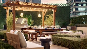 An outdoor dining area with a wooden pergola, string lights, and a table set for a meal.