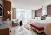 A modern hotel room with a large bed, a sofa, a desk, and a view of the city.