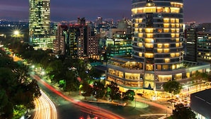 A cityscape at night with illuminated buildings, a roundabout, and light trails from moving vehicles.