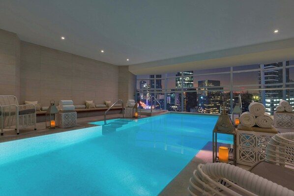 A rooftop infinity pool with city views, lounge chairs, and ambient lighting.