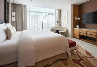 A hotel room with a large bed, a desk, a chair, a TV, and a view of the city.