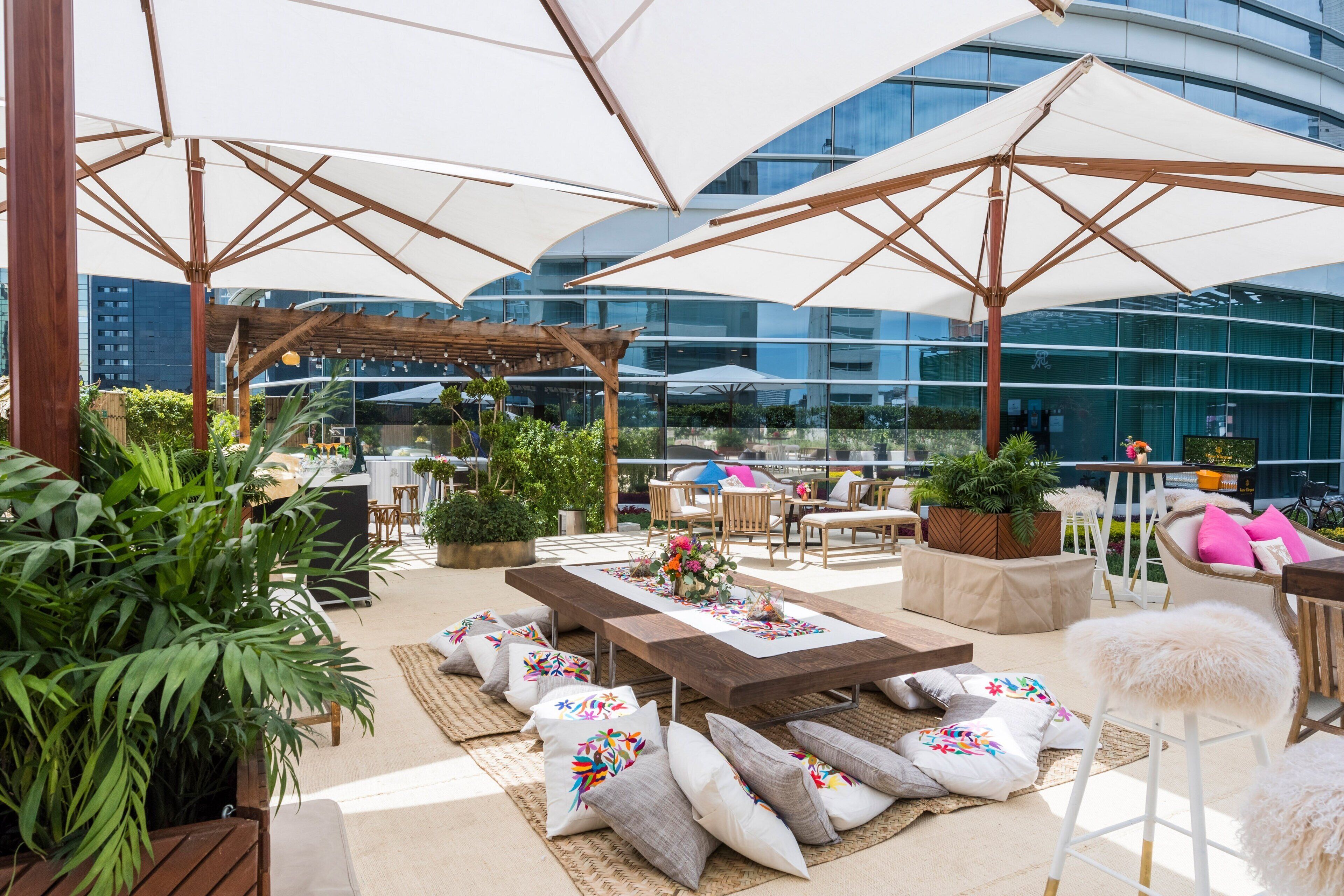 Un patio al aire libre con mesas de madera, asientos acolchados y grandes sombrillas.