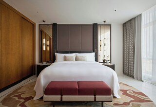 A modern hotel room with a large bed, a bench, a nightstand, and a large mirror.