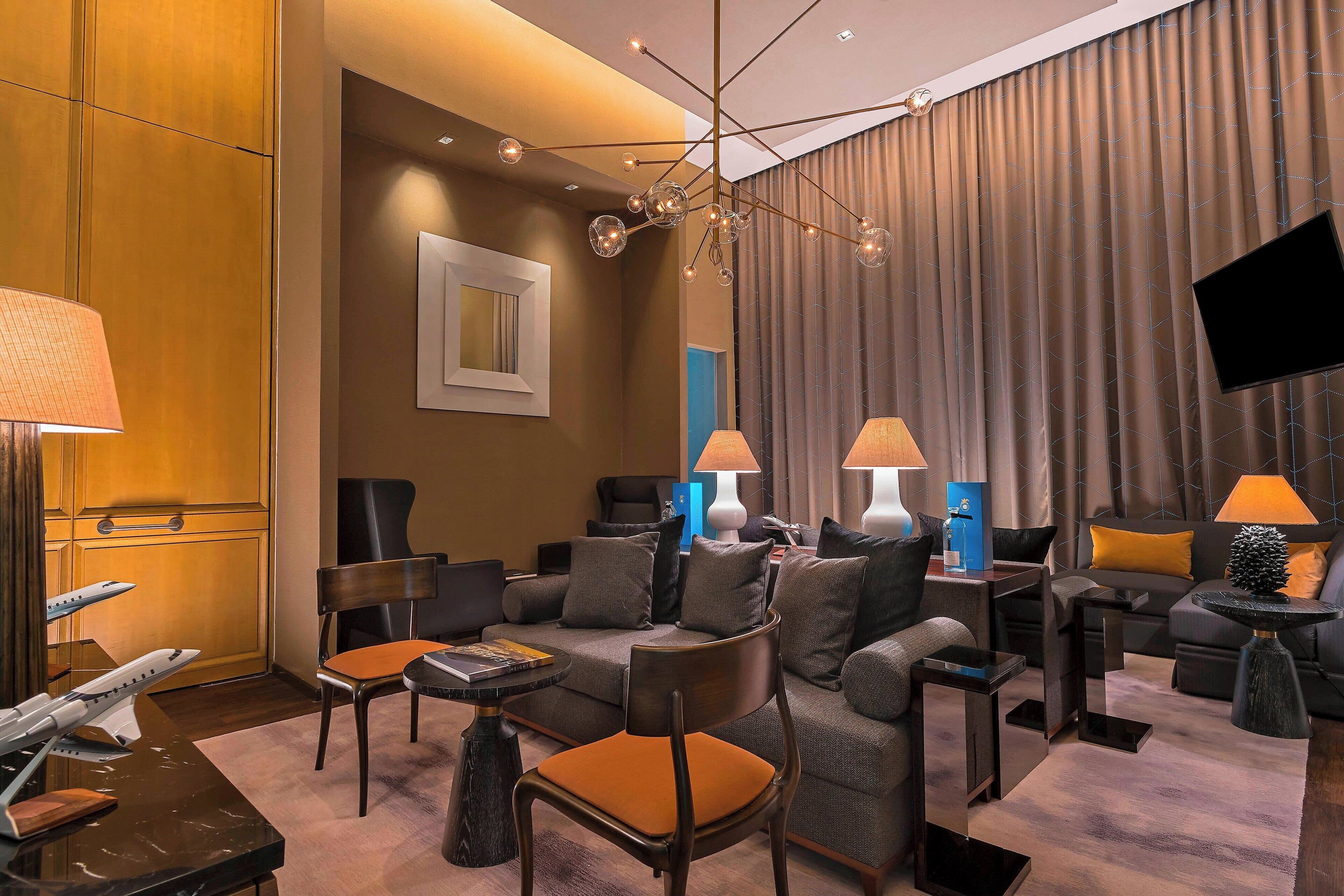 A modern hotel room with a sofa set, a dining table, and a TV mounted on the wall.