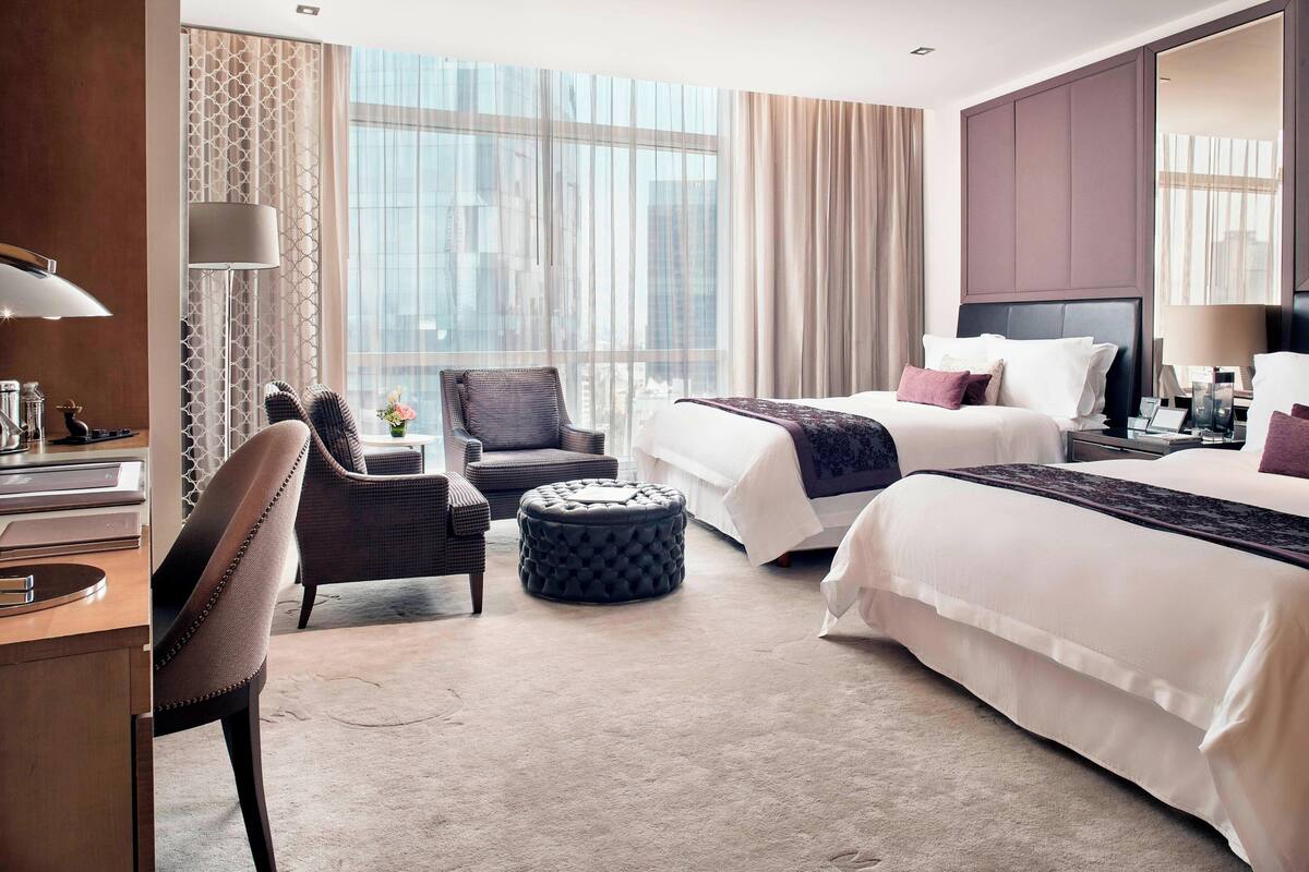 A hotel room with a large window, a bed, a desk, and a chair.