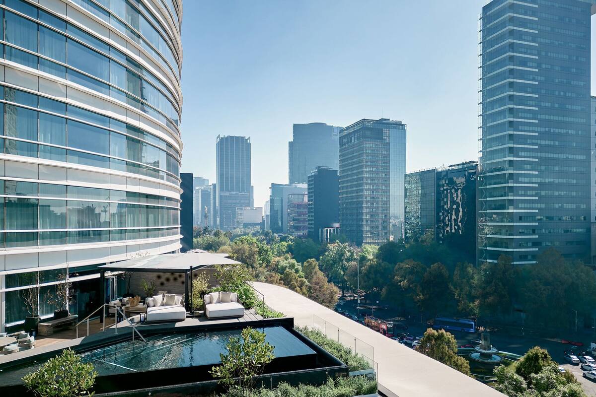 A modern hotel with a rooftop pool, lush greenery, and a view of the city skyline.