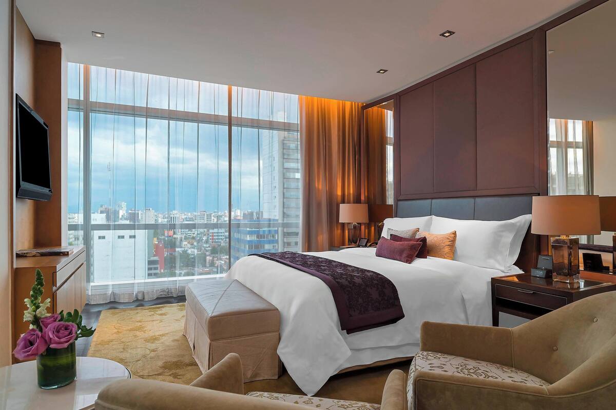 A modern hotel room with a large bed, a TV, and a city view.