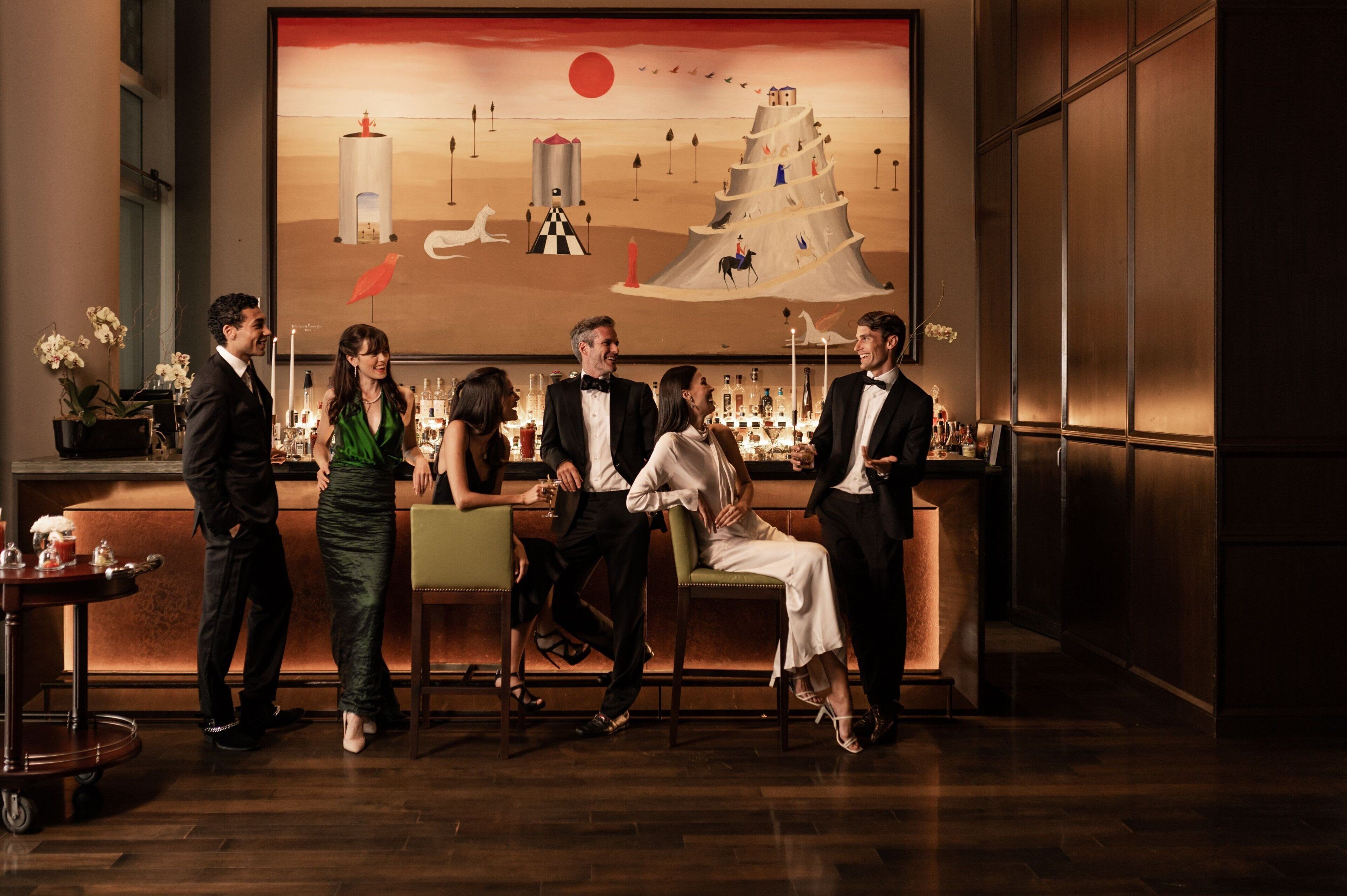 Un grupo de personas con vestimenta formal en un bar con un gran mural de fondo.