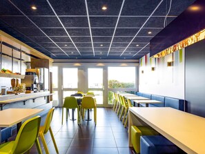 L’intérieur d’un café moderne se caractérise par un plafond à motifs géométriques, une lumière naturelle abondante provenant des fenêtres et des sièges aux couleurs vives.