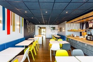 A modern restaurant with high tables and chairs, a counter with food items, and a patterned wall. - ibis budget Quimper (Quimper)