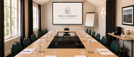Un salón de conferencias con una larga mesa, sillas, una pantalla de proyector y una pizarra.