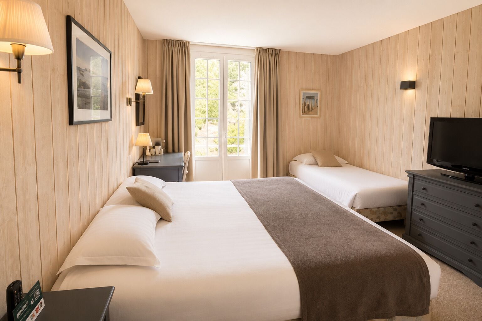Habitación de hotel con dos camas, televisor, escritorio con lámpara y ventana con cortinas.