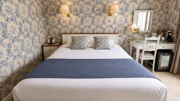 A hotel room with a bed, bedside tables, a desk, a chair, a mirror, and a refrigerator.