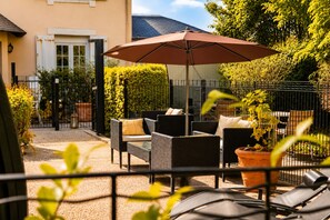 Une terrasse extérieure avec des meubles en osier, un parasol marron et des plantes en pot.