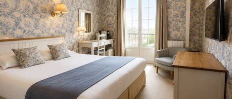 A hotel room with a large bed, a desk, a chair, a TV, and a balcony view.