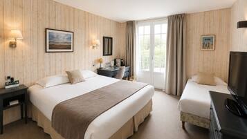 A hotel room with a large bed, a smaller bed, a desk with a lamp, a television, and a window with curtains.