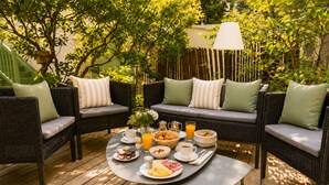 A patio with wicker furniture, a round table with breakfast items, and a lamp. - Hôtel Villa Flornoy Pornichet Baie de la Baule (Pornichet)