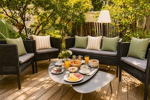 A patio with wicker furniture, a round table with breakfast items, and a lamp. - Hôtel Villa Flornoy Pornichet Baie de la Baule (Pornichet)