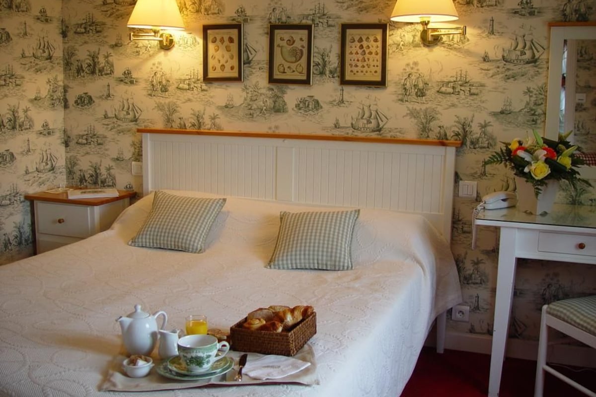 Un lit bien fait, avec des oreillers, une table de chevet avec une lampe et un plateau de petit-déjeuner posé sur le lit.