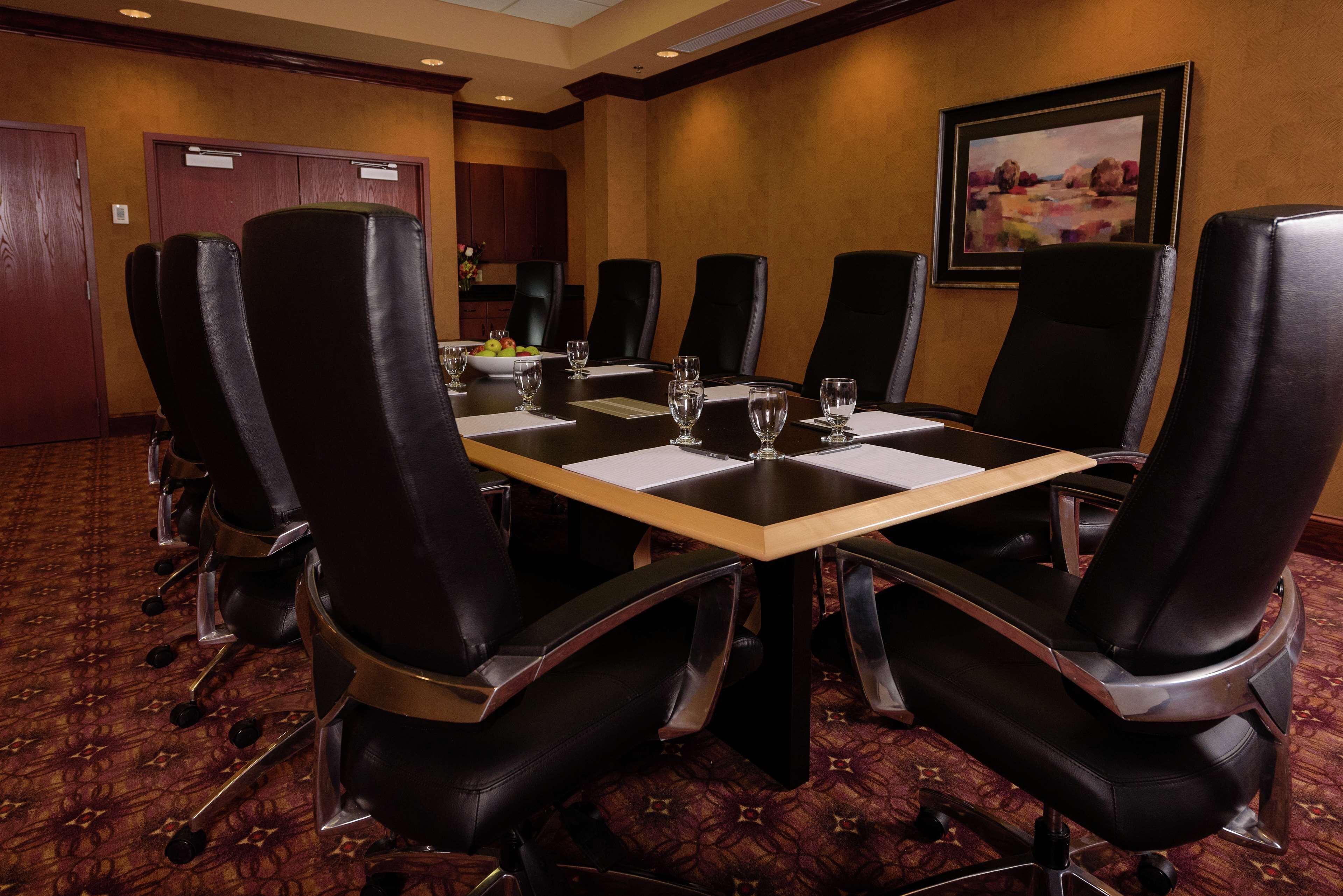 A conference room with a rectangular table, black leather chairs, and a carpeted floor.
