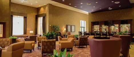 Un vestíbulo de hotel con varias zonas de estar, un bar y una recepción.