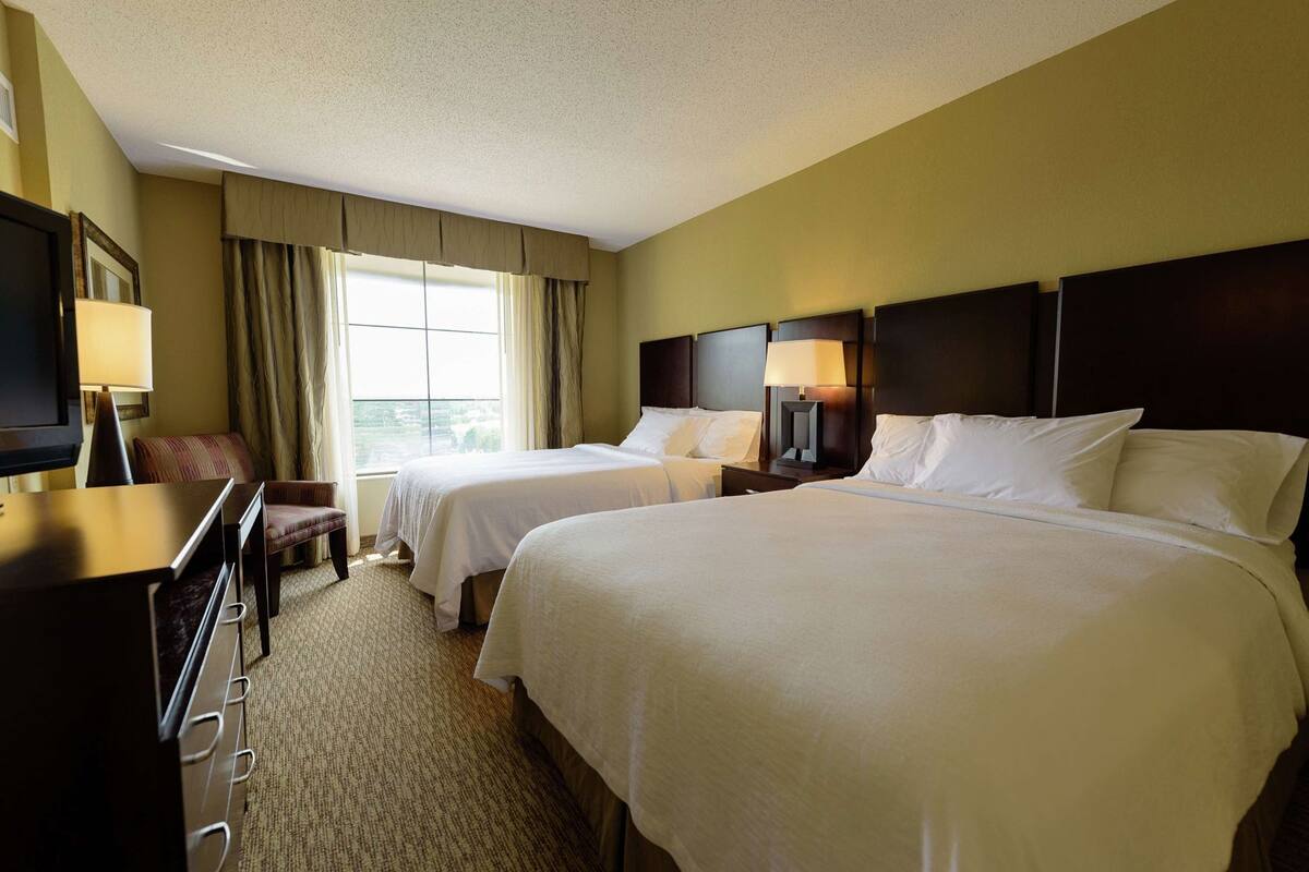 A hotel room with two beds, a desk, a chair, and a television.
