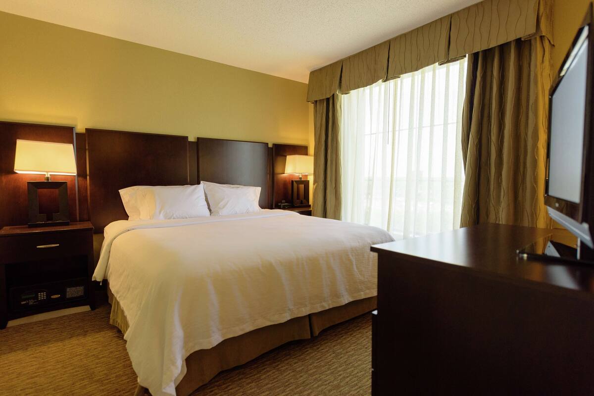 A hotel room with a large bed, two bedside lamps, a desk, and a television.