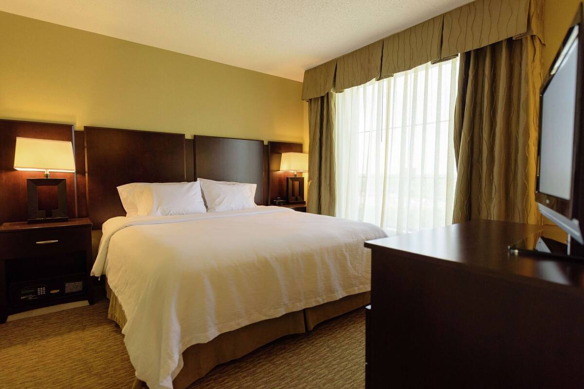 A hotel room with a large bed, two bedside tables with lamps, a desk, and a television.
