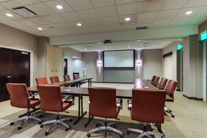 A conference room with a long table, multiple chairs, a projector screen, and an exit sign.