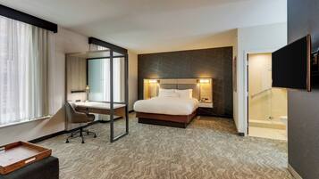 A hotel room with a bed, desk, chair, and a TV on the wall.