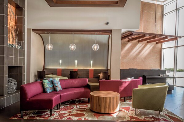 A modern lounge area with a red sofa, round wooden coffee table, and a large window providing natural light. - SpringHill Suites Birmingham Downtown at UAB (Birmingham)